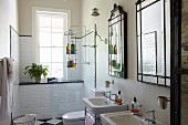 Twin washstands below framed mirrors on wall; shower area next to window with white wall tiles in background