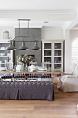 Comfortable dining area with upholstered armchairs and bench with grey loose cover below vintage pendant lamps with metal lampshades