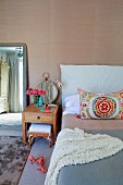 Colourful, ethnic scatter cushion on bed and solid wood bedside table against wall