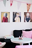 Gemalte Kinderportraits über schwarzem Polstersofa mit rosafarbenem Kissen und weißem Tisch