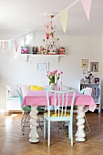 Massiver, weisser Esstisch mit gedrechselten Beinen mit rosa-weiss gepunkteter Tischdecke im Esszimmer mit pastellfarbener Wimpelgirlande dekoriert