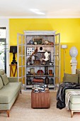 Fifties-style, pale green sofa set and wooden table in front of display cabinet with open doors and view of antique collectors' items in living room with yellow-painted wall