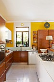 Open-plan kitchen with white island counter, wooden fitted cabinets and yellow-painted walls
