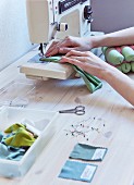 Colourful fabric samples and pins next to sewing machine; woman's hands holding fabric under sewing machine needle