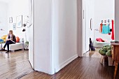 Hallway with open doors; woman sitting in living room and coat rack on wall above pouffe