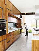 Woman opening oven in spacious designer kitchen with exotic wooden fronts