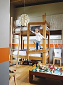 Junge am Hochbett kletternd; orangefarbene Wandstreifen und Aststrukturen an der Wand