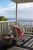 Towel draped over pale wicker chair and basket on sunny wooden deck with sea view