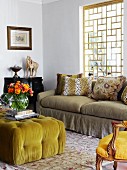 Ottoman with lime green cover and colourful bouquet in vase opposite sofa below window with wooden lattice framework