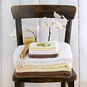 Handtücher, Seife und Badebürste auf einem Holzstuhl vor Orchidee