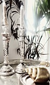 Zwei silberne Kerzenständer mit Verzierungen auf Tablett, im Vordergrund Deko-Schneckenhaus