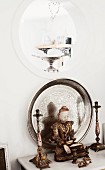 Buddha figurine flanked by candlesticks in front of silver tray leaning against wall below porthole aperture