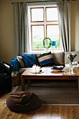 Wooden coffee table, sofa with striped scatter cushion and brown bean bag in front of window in rustic interior