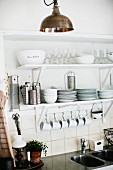 Crockery and glasses on white bracket shelves with cups hanging from row of hooks
