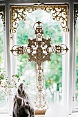 Ornate crucifix made from white-painted metal in front of window