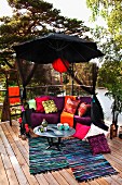 Colourful relaxation area on terrace below black parasol with red lantern and view of trees and lake