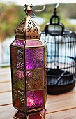 Bronze-coloured, Oriental-style metal lantern with coloured glass panels on wooden terrace