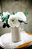 weiße Rosen in Porzellankrug auf Beistelltisch mit Spitzendeckchen