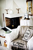 Armchair with lace blanket and printed linen throw in front of open fireplace in rustic interior