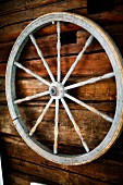 Old cart wheel with turned spoked hanging on wooden wall