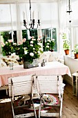 Weathered, wooden folding chairs painted white in front of potted plants on tablecloth on table in corner of loggia