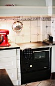 Schwarzer Vintage Küchenherd vor weissen Fliesen mit Einlegern an Wand, in schlichter Küche