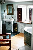 Vintage, pedestal sink on column-style legs next to window with painted interior shutters in bathroom with wooden and tiled floor