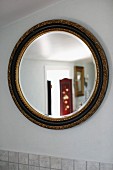 Round mirror with gilt frame on white wall