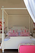 Himmelbett mit weißem Holzgestell und pink-weiss gemusterten Kissen