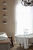 Free-standing vintage bathtub in front of window with lace curtain