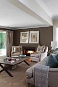 Pale armchairs with scatter cushions and sofa around coffee table on sisal carpet; open fire in brown-painted wall of living room