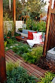 Terrace with wooden decking between beds of ornamental grasses and bench with cushions