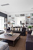 Black sofa set around wooden coffee table in living room with white fitted shelving in background