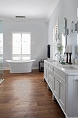 Waschtisch mit Doppelbecken und weissen Unterschränken im Landhausstil, im Hintergrund freistehende Badewanne vor französischem Fenster