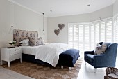 Elegant white bedroom with blue accents, blue armchair and blue bench at foot of bed