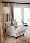 Pale armchair with striped scatter cushion next to standard lamp with lettering on lampshade