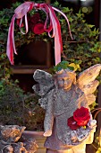 Stone angel lit from one side in front of ivy wreath in garden