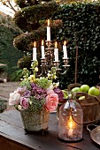 Candle lantern and flower arrangement in front of candelabra on rustic garden table