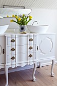 Vintage chest of drawers converted into washstand with twin countertop basins; vase of yellow tulips