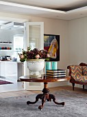 Antiker, runder Tisch mit grossem Pflanzgefäss und Proteastrauss im Wohnraum, vor offener Flügeltür und Blick in die Küche