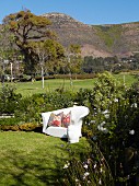 White, outdoor sofa with ethnic scatter cushions in sunny garden in front of mountain landscape