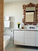 Blick durch offene Tür auf modernen Waschtisch mit weißem Unterschrank, Wandspiegel mit verziertem Holzrahmen