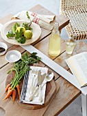 Cutlery and vegetables on wooden board next to lemonade and lemons on wooden table