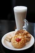 Three different biscuits on a plate with a latte macchiato in the background