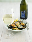 A glass of white wine with a mussel dish and a bottle of wine in the background out of focus