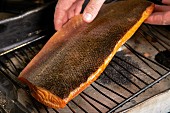 A chef placing a pan-smoked salmon fillet on a wire cooling rack