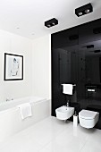 Toilet and bidet mounted on black glass wall and large, white floor tiles in designer bathroom