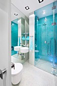 Waschbecken an vollflächigem Wandspiegel montiert, neben verglastem, bodenebenem Duschbereich mit hellblauen Mosaikfliesen an Wand