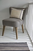 Striped linen cushion on retro easy chair with taupe upholstery; striped, woven rug in foreground