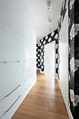A crocked hallway with shiny, built-in cupboards and black and white floral wallpaper